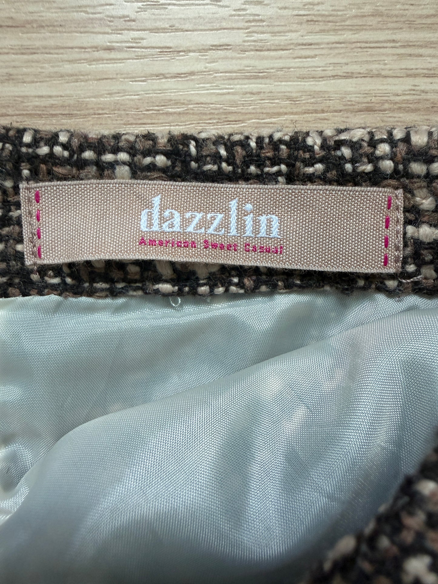 Close-up of a garment label reading 'dazzlin American Sweet Classic' sewn onto a tweed trim, with a light satin lining visible below.
