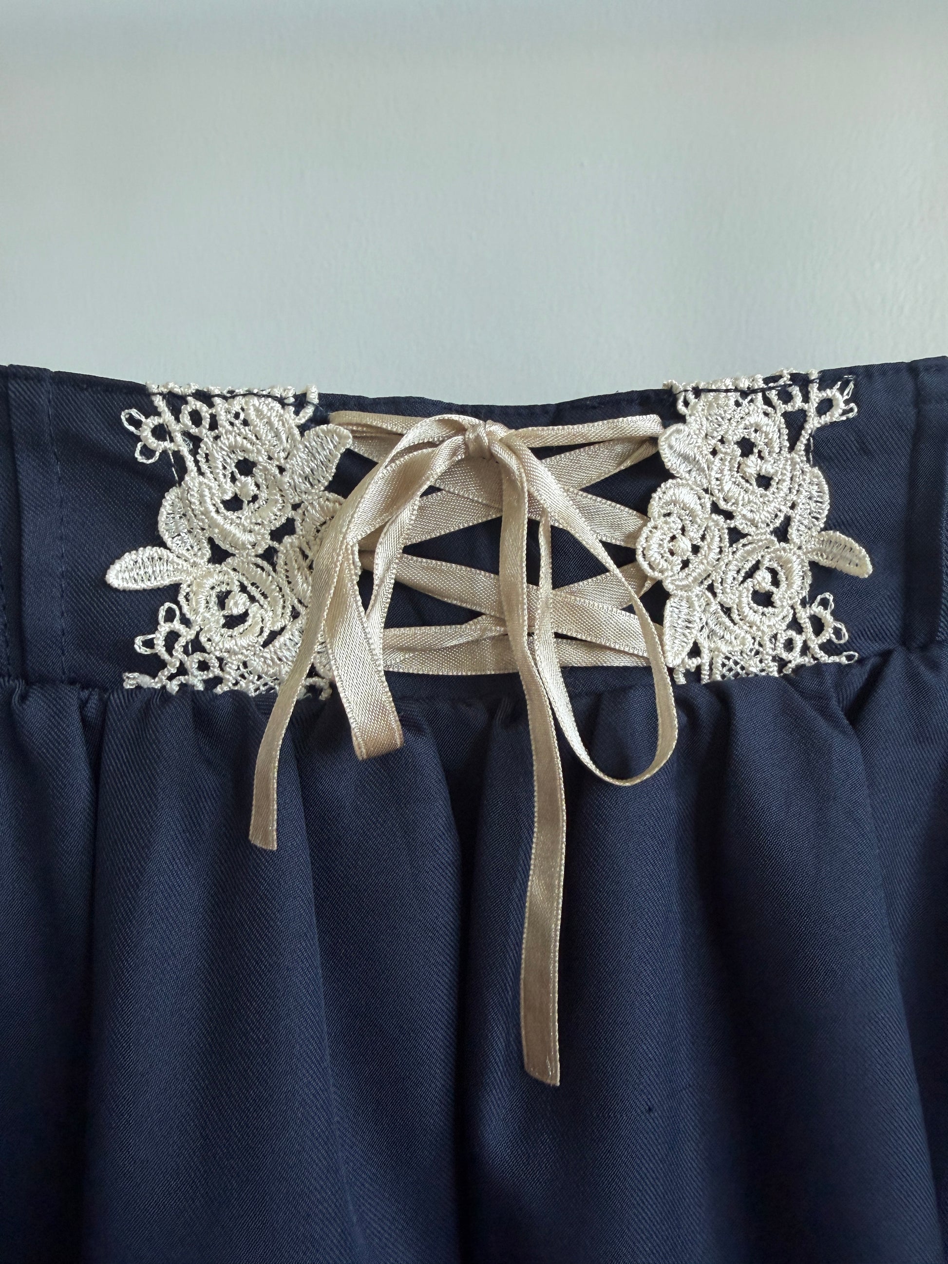Close-up of a navy blue skirt with white floral lace applique and beige ribbon laces at the waistband.