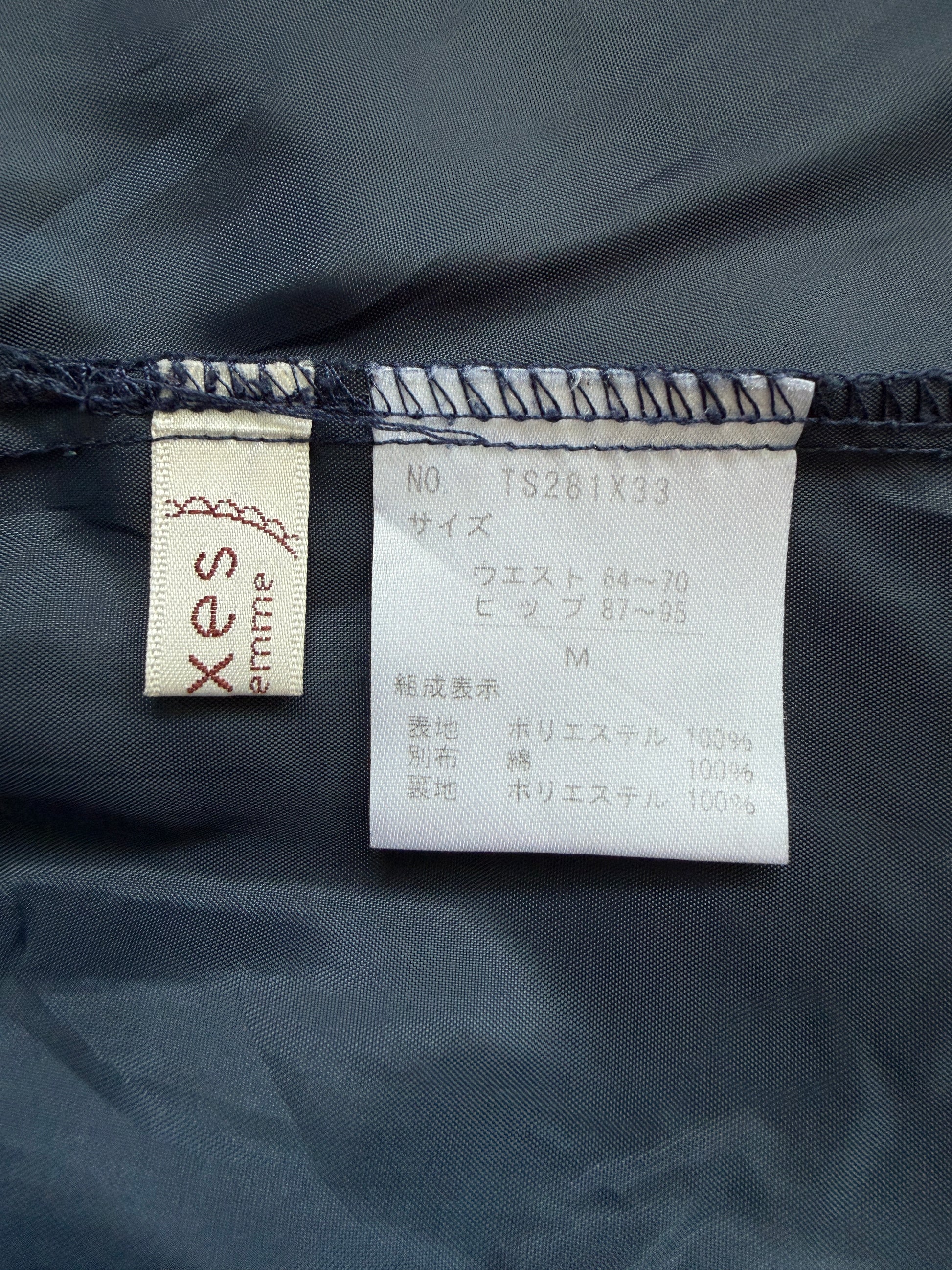 Close-up of a garment's interior labels showing the brand 'xes entrie' on a beige tag and size information on a white tag, set against dark navy blue fabric.