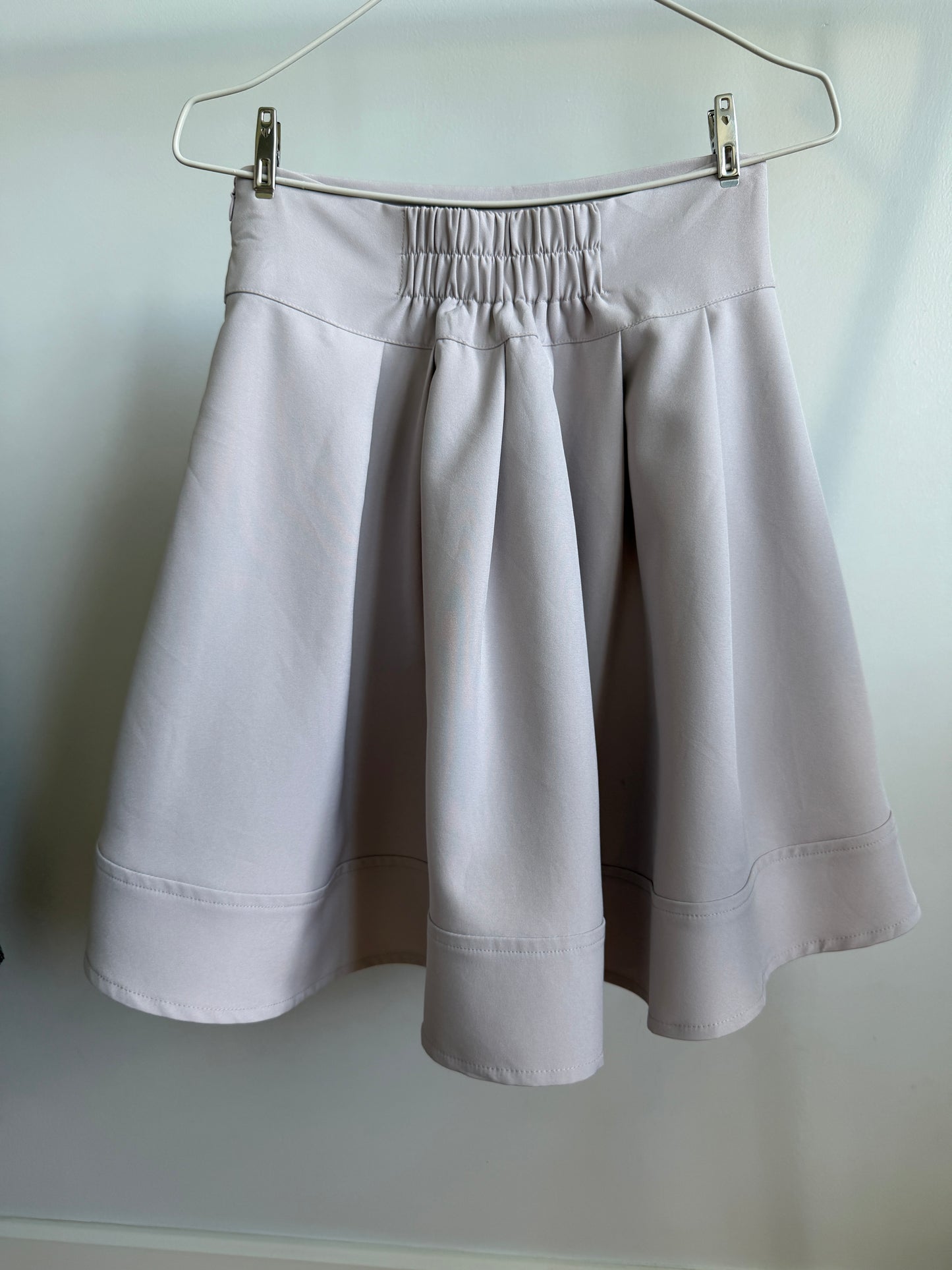 A light gray pleated skirt with an elastic waistband, hanging from a metal hanger against a plain light background.