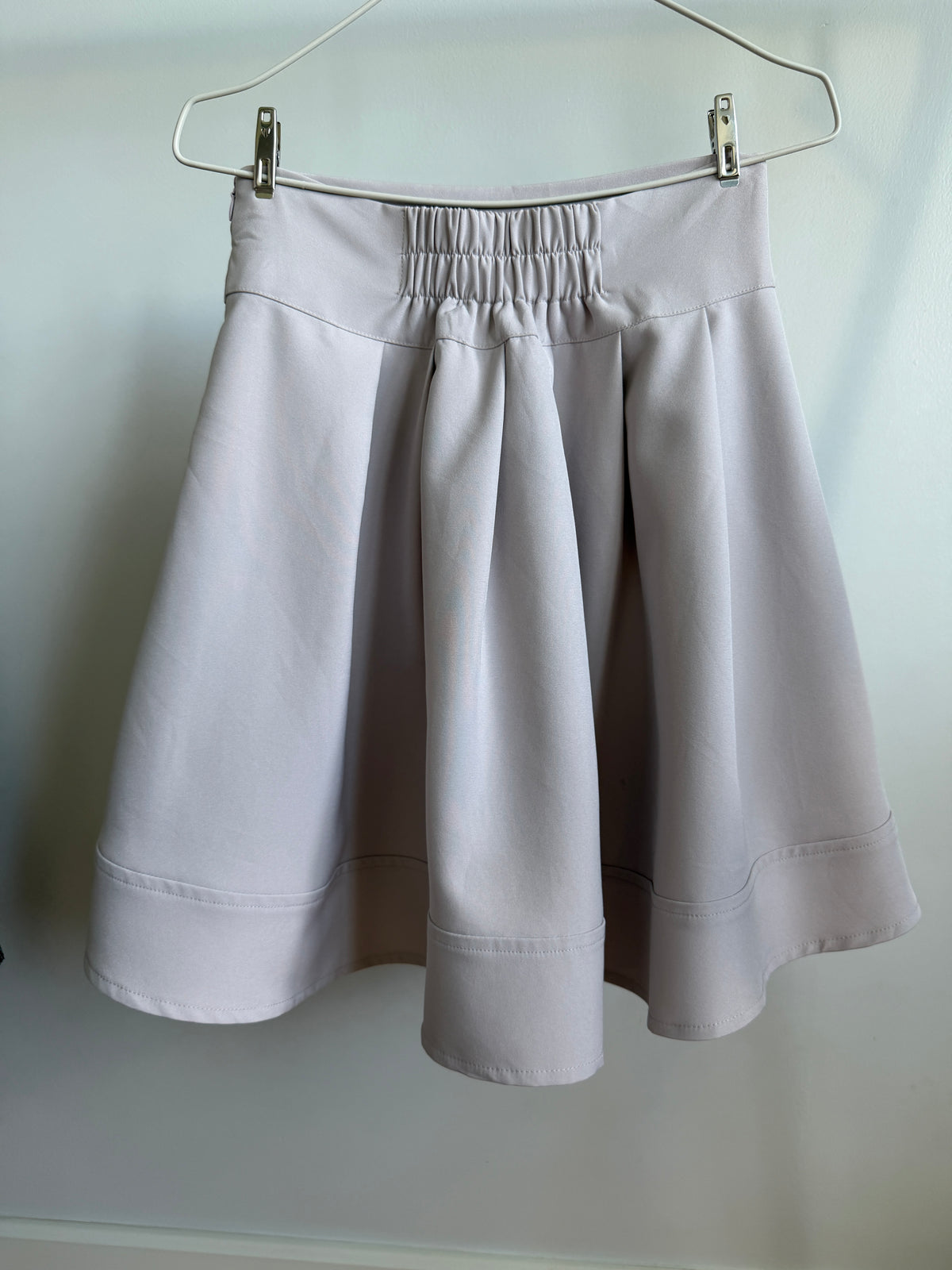 A light gray pleated skirt with an elastic waistband, hanging from a metal hanger against a plain light background.