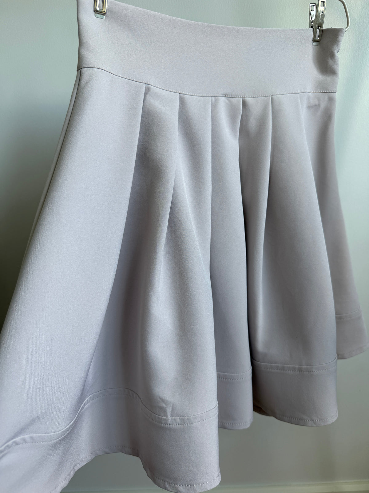 A light gray pleated skater skirt hanging from a metal hanger against a plain light background.