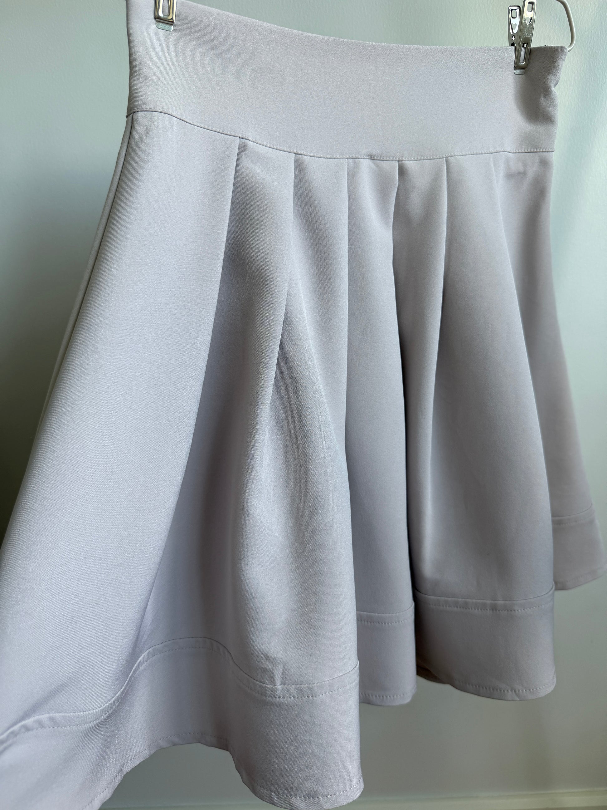 A light gray pleated skater skirt hanging from a metal hanger against a plain light background.