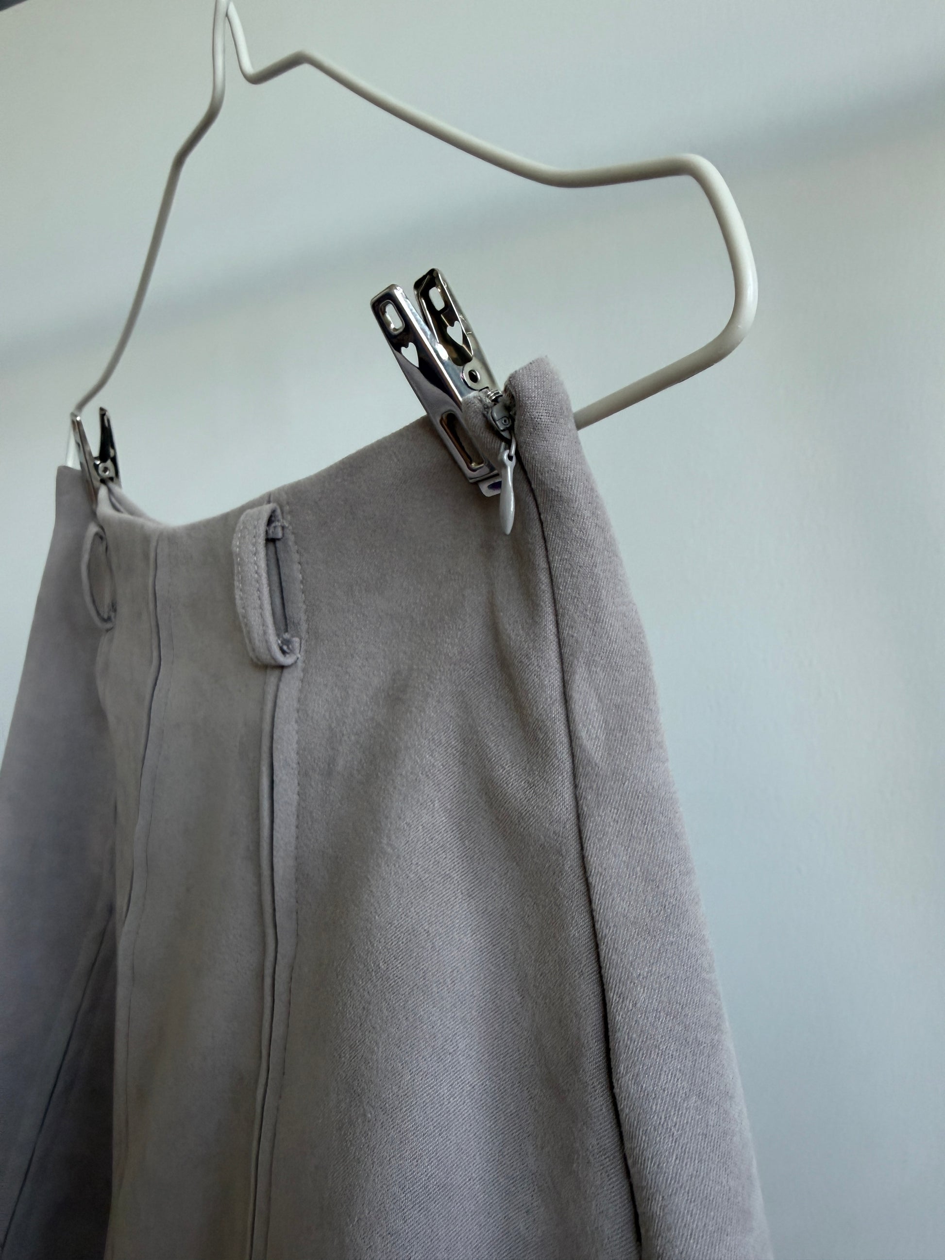 A close-up of a light gray wool or cashmere garment clipped to a white hanger against a plain light gray wall.