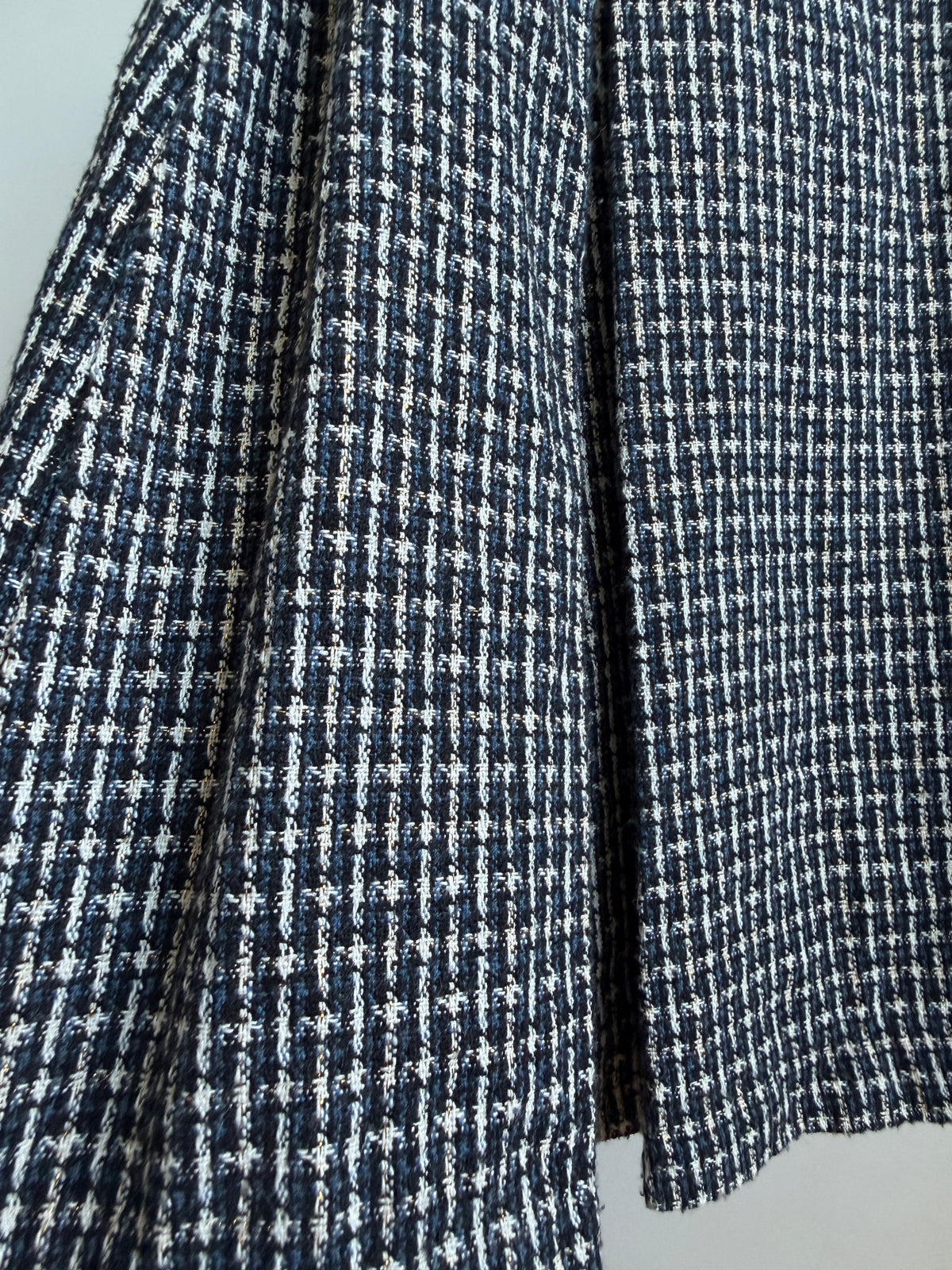 Close-up of a navy and white micro-check patterned fabric, likely tweed or woven wool, showing the texture and folds.