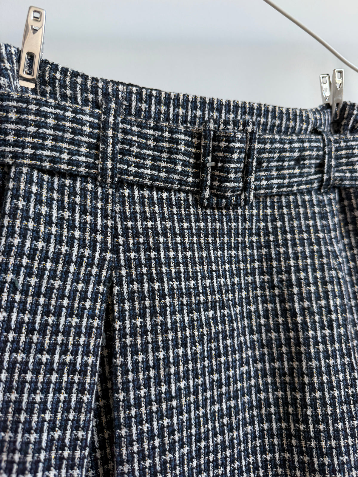 Close-up of a houndstooth patterned skirt in navy blue and white, hanging from silver metal clips against a light gray background.