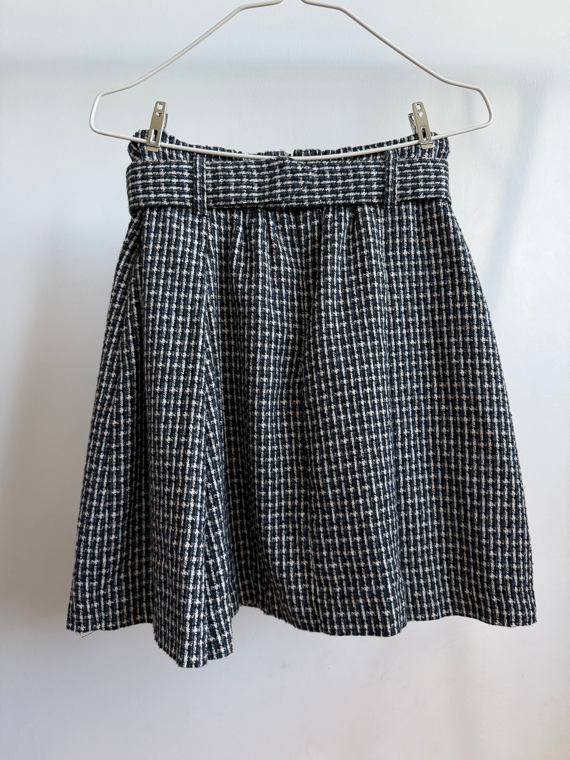 A black and white houndstooth patterned skirt hanging from a metal hanger against a plain white wall.