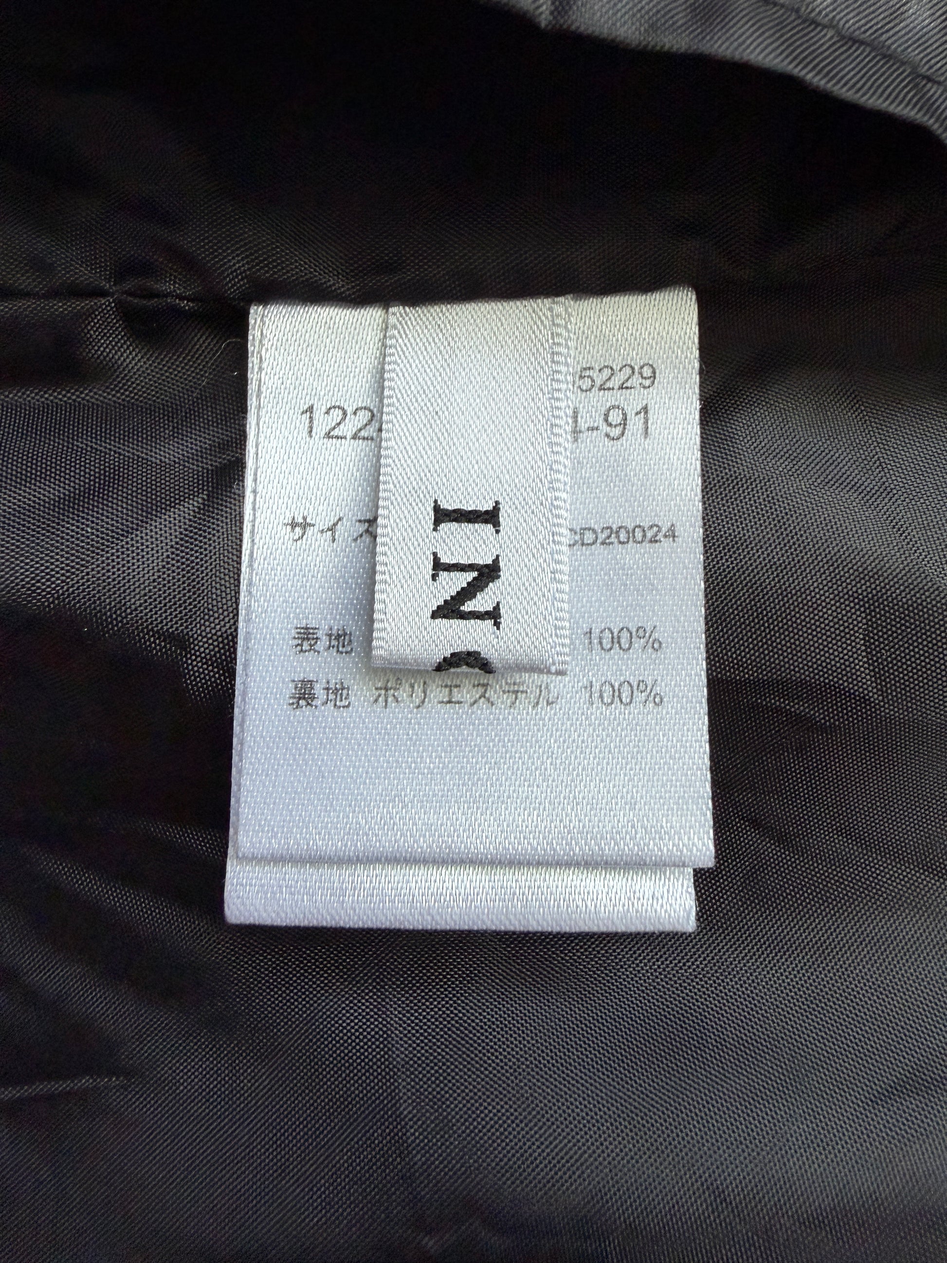Close-up of a white fabric garment tag sewn onto a black puffer jacket, showing Japanese size and material information.