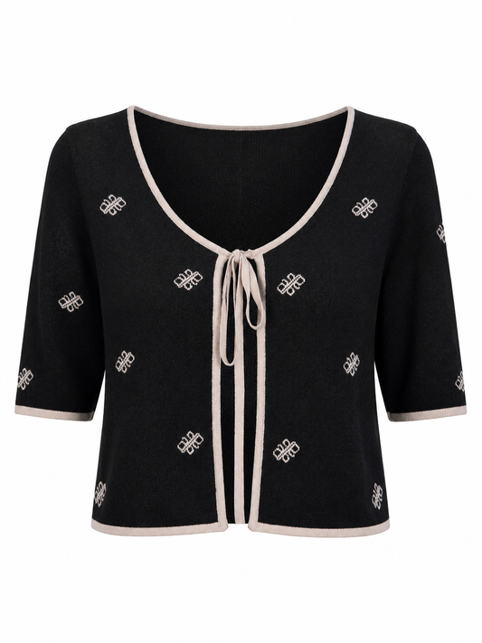 A black knit top with a boat neckline, elbow-length sleeves, and a repeating white geometric logo pattern. The top features tie in the middle, light beige trim along the collar, cuffs, and hem, shown against a plain white background.