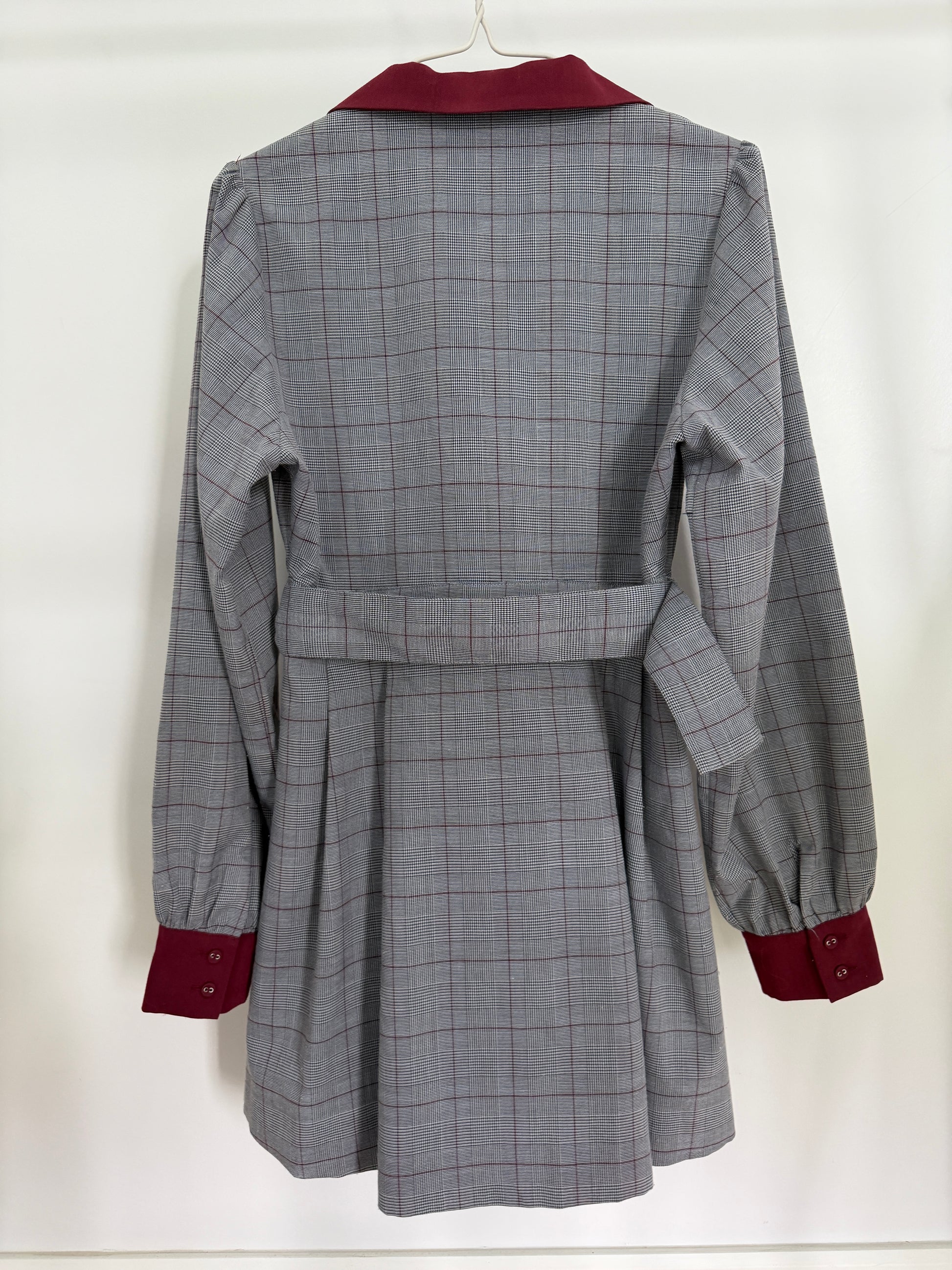 A gray and white plaid belted coat with contrasting dark red collar, cuffs, and button details, hanging on a white hanger against a white background.